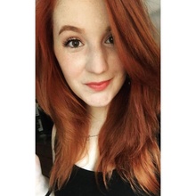 Woman with long red hair and a black shirt smiling with her lips closed into the camera