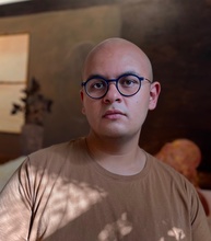 Man in a brown shirt wearing spectacles.