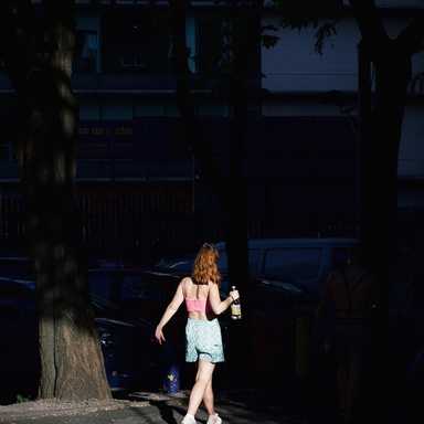 Woman walking through a dimly lit street holding a bottle