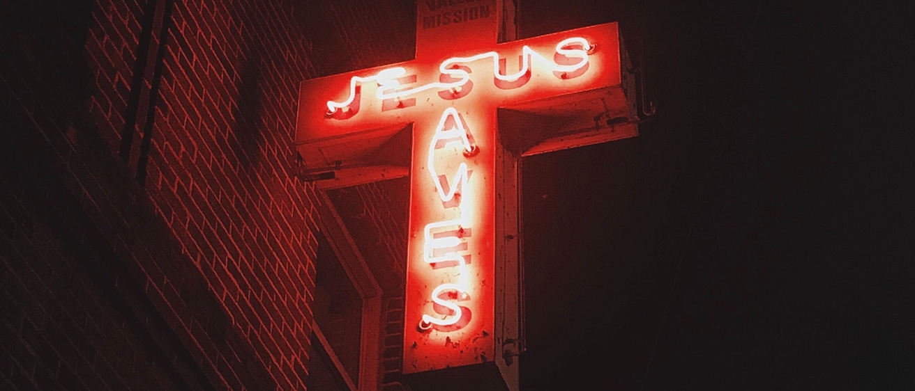 neon sign reads "Jesus saves" on a cross