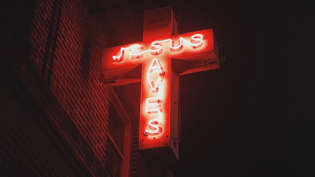 neon sign reads "Jesus saves" on a cross